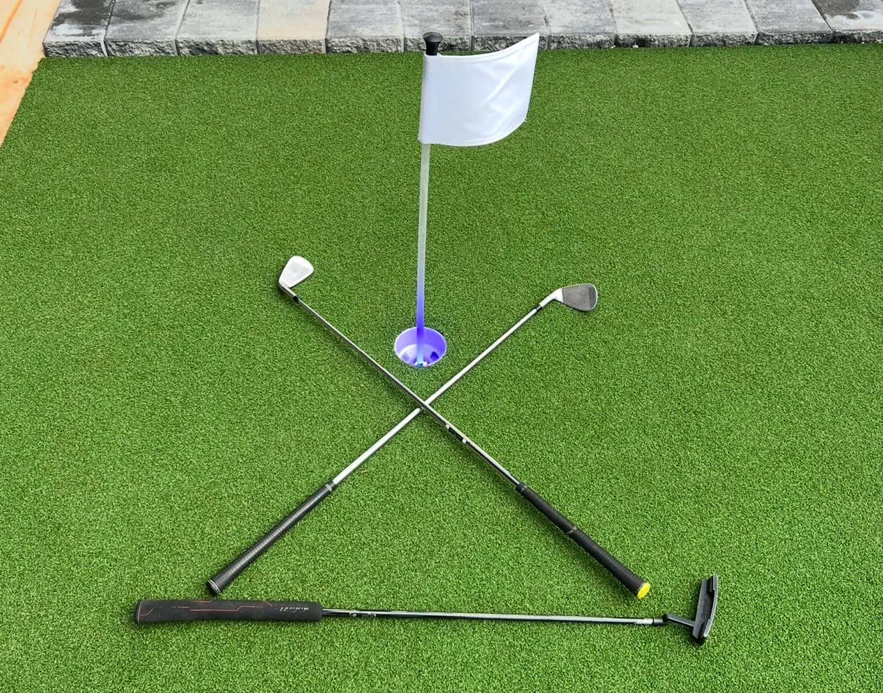 Two golf clubs crossed on green artificial turf with a golf hole and flag in the center.