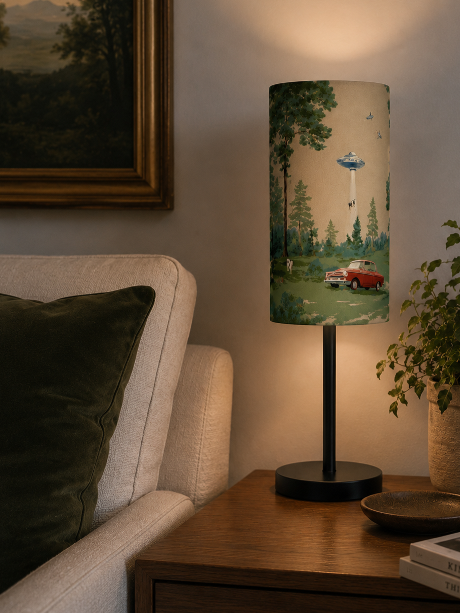 A nightstand with a lamp featuring a vintage car and forest scene, next to a beige couch and a plant, in a cozy living room.