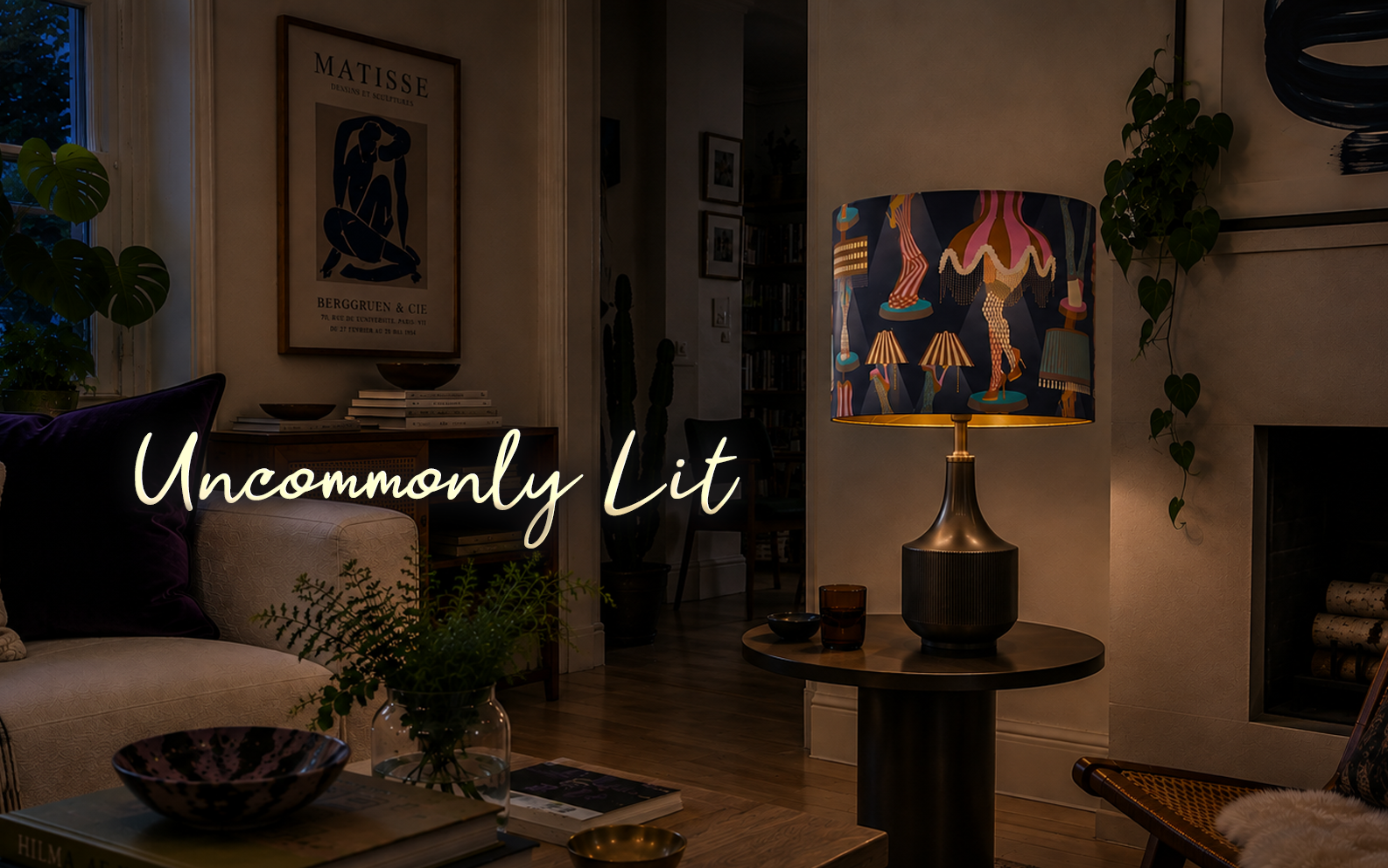 A cozy living room with a lamp on a side table, modern artwork, a couch with purple pillows, and indoor plants, illuminated by warm lighting and featuring the text 'Uncommonly Lit' over the scene.