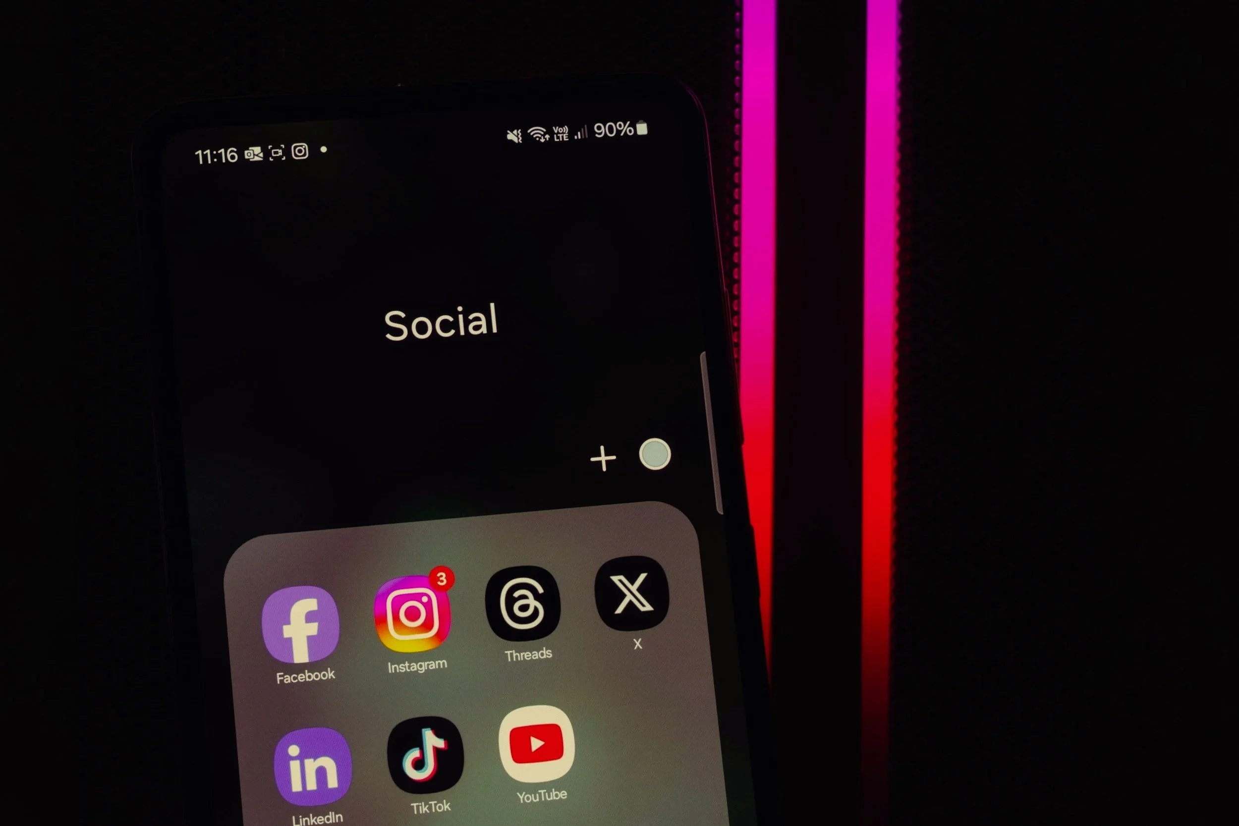 A smartphone screen displaying social media and messaging app icons with the word 'Social' on the screen, set against a black background with pink and red lines.
