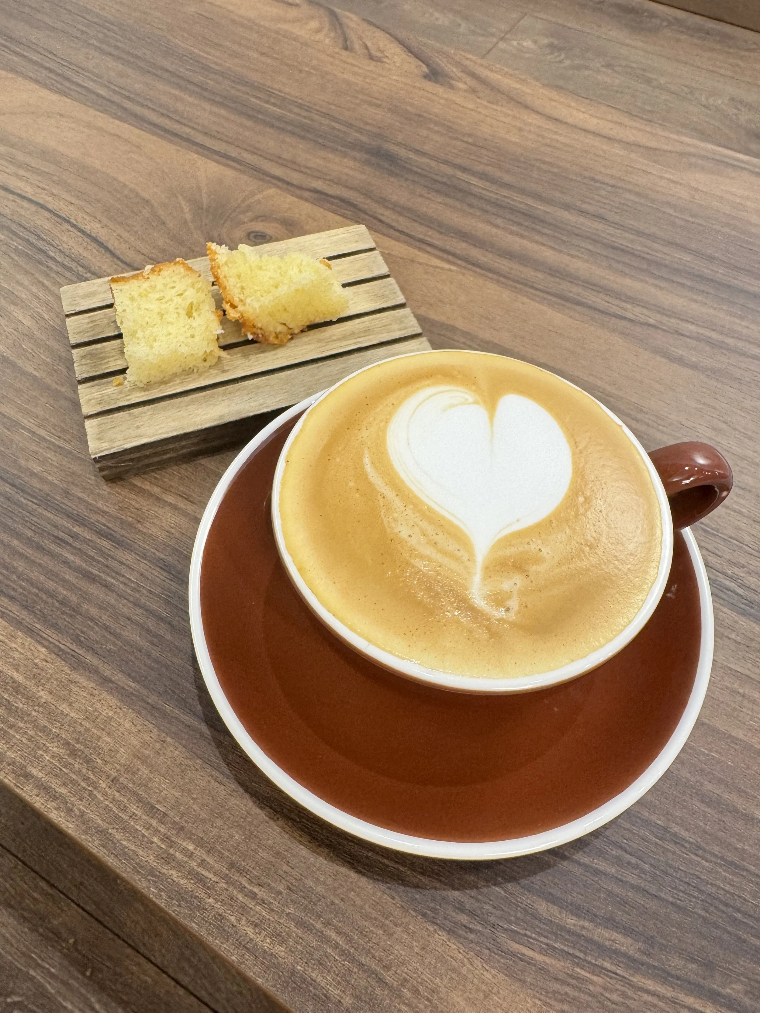 A cup of caramel latte with foam art on top and two pieces of sponge cake on a wooden table.