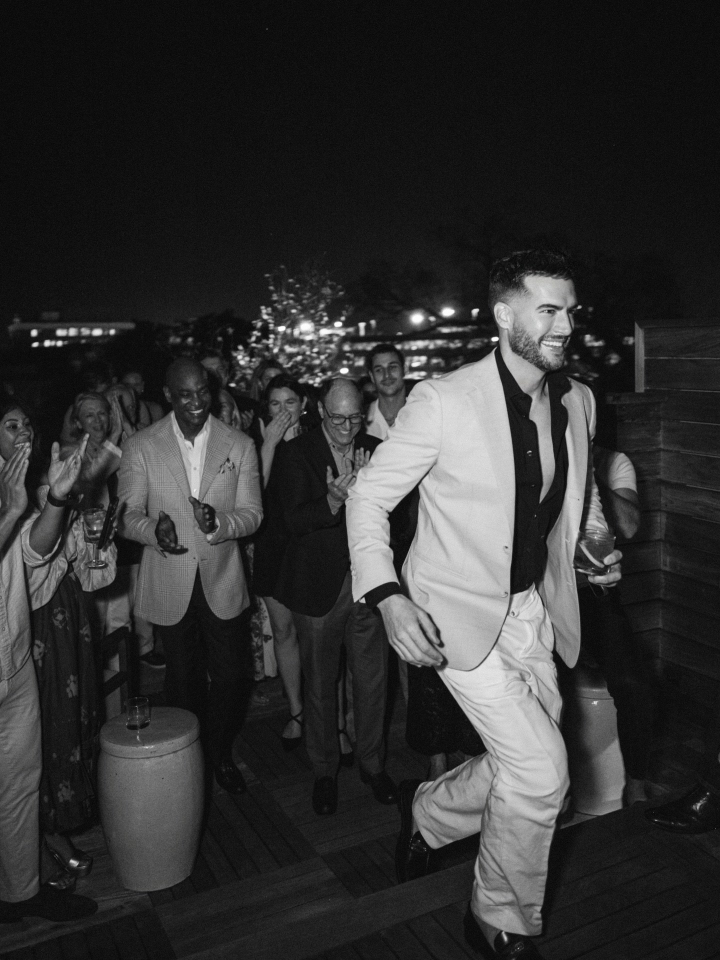 Black-and-white photograph of Ryan walking up a staircase with a group of people gathered behind him at a celebration.