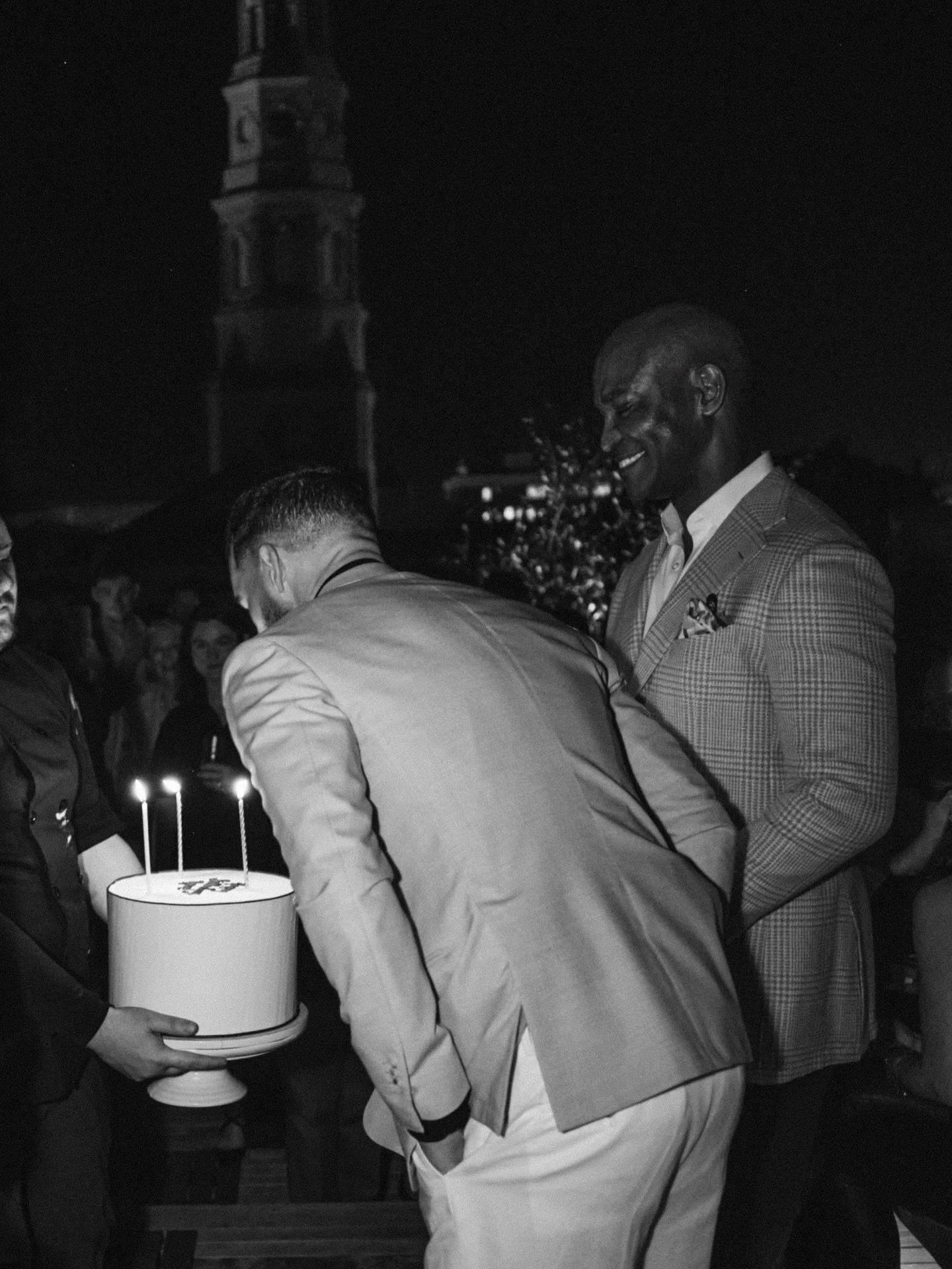 Black-and-white photograph of Ryan and his husband celebrating together as Ryan blows out the candles on a cake.