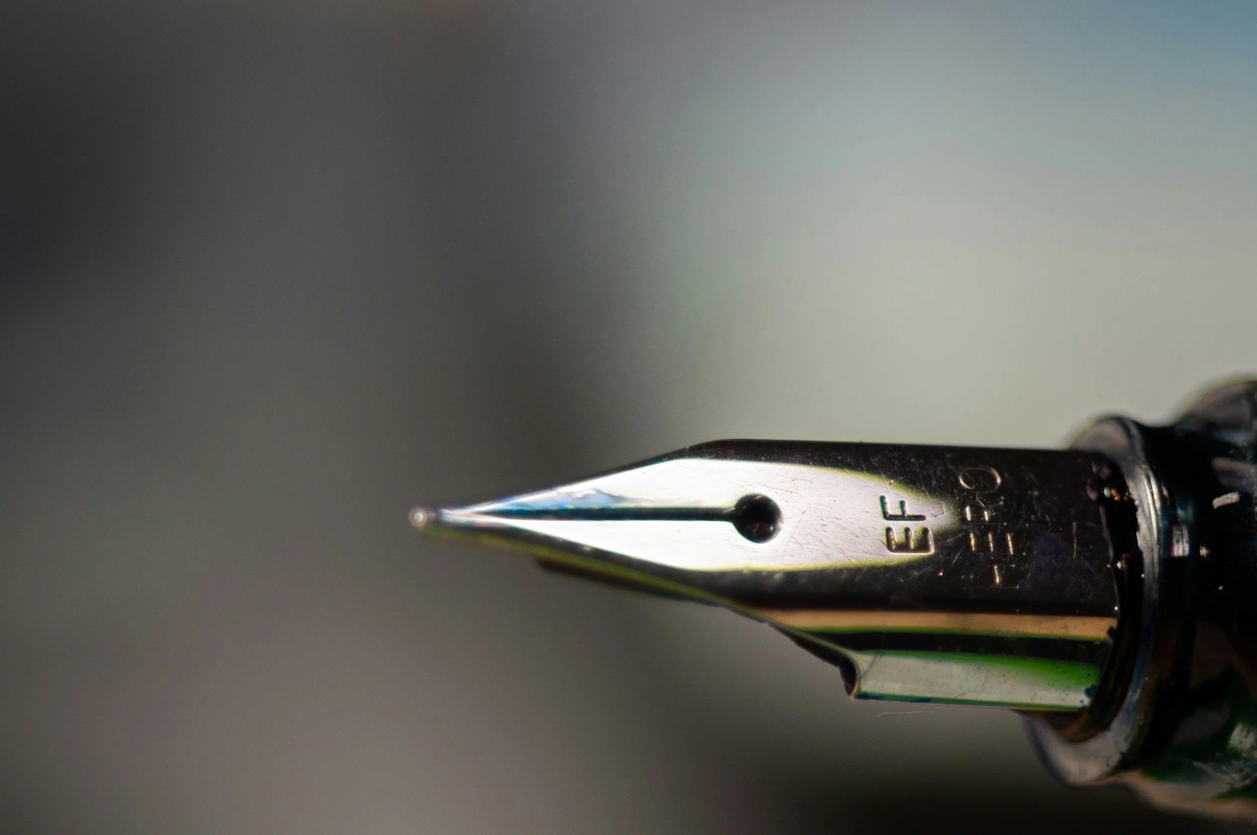 Close-up of a metallic fountain pen nib with engraved text, against a plain background.