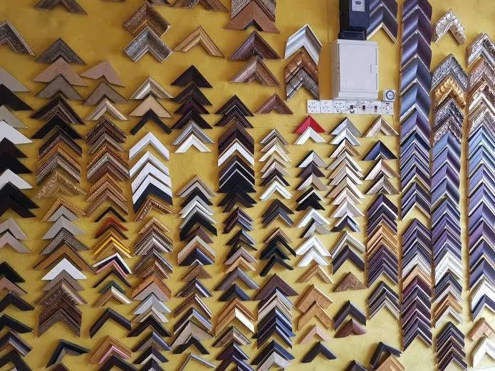 Display of various picture frame samples arranged on a yellow wall.
