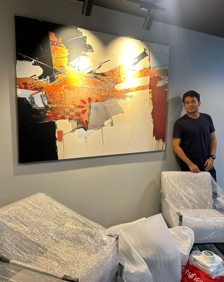 A man in a black t-shirt standing next to covered furniture in a room with a large abstract painting on the wall.