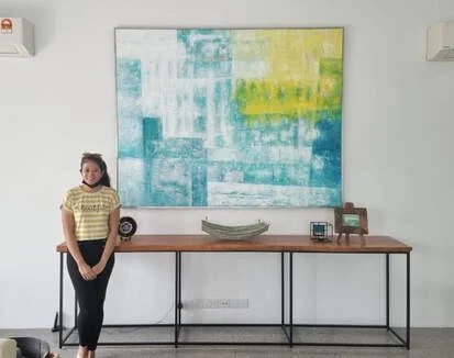 Woman standing next to a wooden console table with decorative items in front of a large abstract painting.