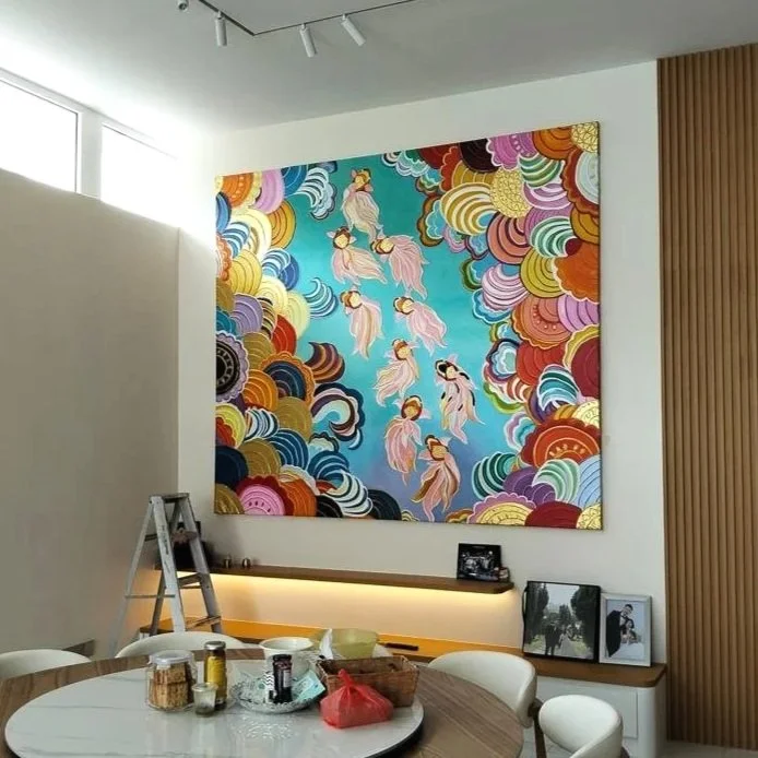 Colorful modern wall art depicting dancers in flowing pink and white dresses among swirling cloud-like patterns in shades of blue, pink, orange, and gold, in a bright interior room.