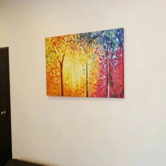 Colorful abstract painting of trees on a white wall.