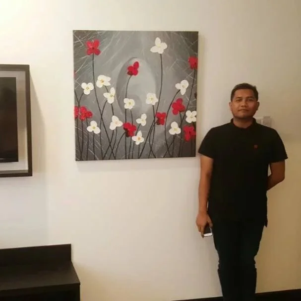 A man standing in front of a floral painting with red and white flowers on a gray background inside a room.