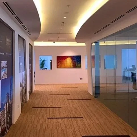Modern office corridor with artwork on white wall, glass wall on the right, and hardwood floors.
