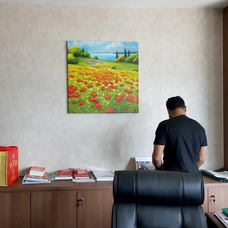Man standing in front of a desk with books and a laptop, with a colorful landscape painting on the wall behind him.