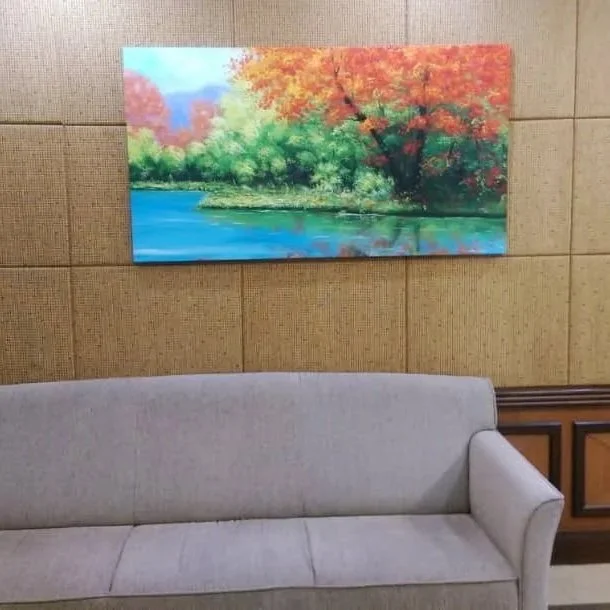Framed landscape painting of a river and trees with colorful fall foliage hanging on a textured wall above a light gray sofa.