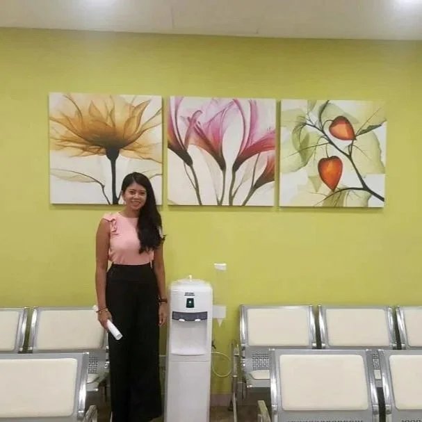 A woman standing in a waiting area with a water cooler, colorful flower artwork on a lime green wall, and empty chairs.