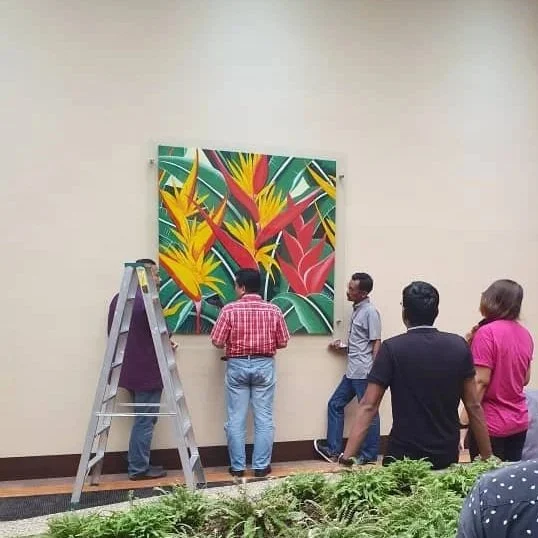 People examining or discussing a colorful tropical-themed painting of birds and plants on a wall.