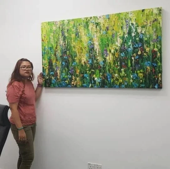 A woman standing next to an abstract colorful painting on a white gallery wall.