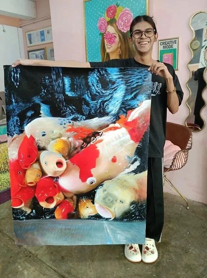 Person holding a colorful tapestry with koi fish and ceramic lanterns, standing in an art studio with pink walls and framed artwork.
