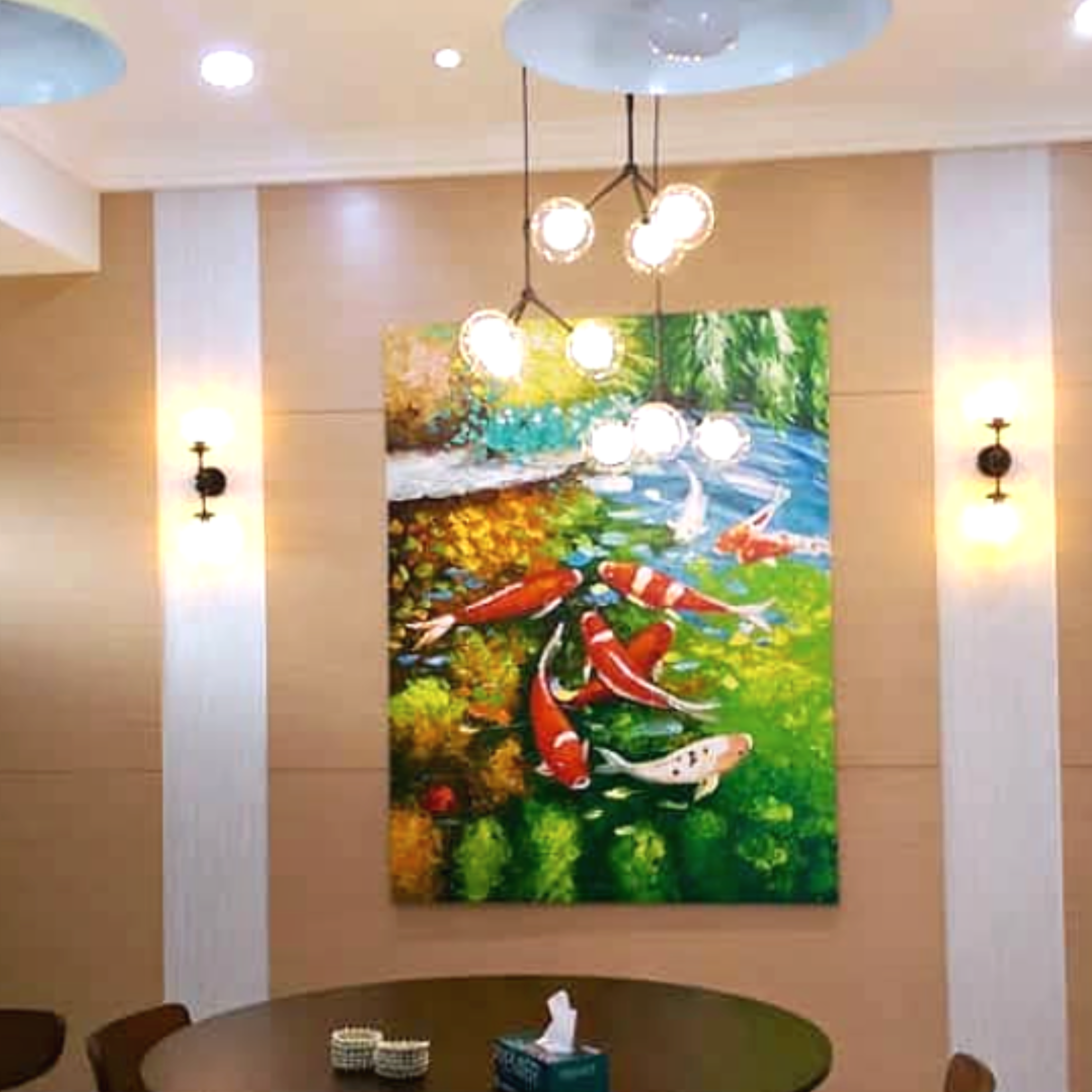 A room with a round green table surrounded by chairs, a hanging light fixture with multiple bulbs, and a colorful landscape painting on the wall.