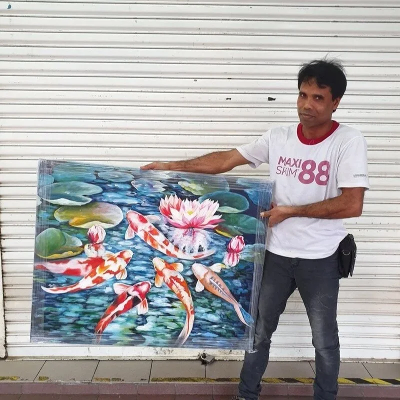 A man holding a framed painting of koi fish swimming in a pond with water lilies.