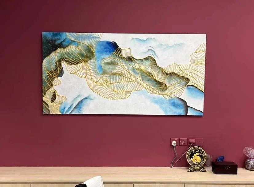 Abstract watercolor painting with gold accents hanging on a maroon wall, with a wooden surface below holding various decorative items.