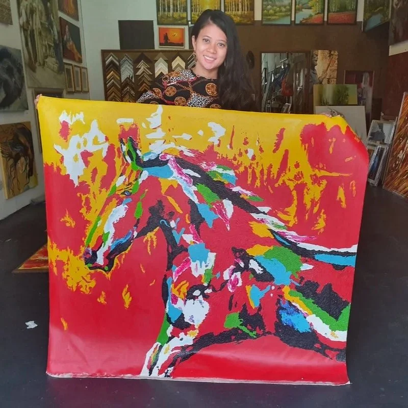 A woman holding a colorful abstract painting inside an art gallery.