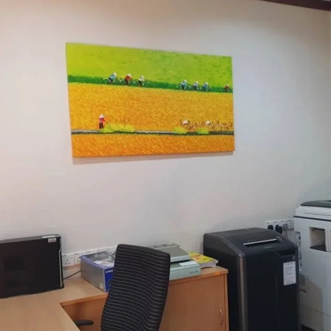 Colorful painting of farmers working in a vibrant green and yellow field, hanging on an office wall.