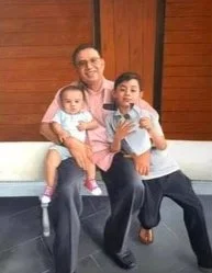 A man with two children sitting outdoors on a bench, smiling at the camera.