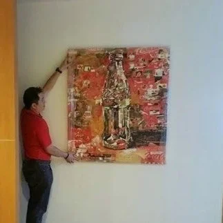 Person hanging an abstract painting on a white wall.