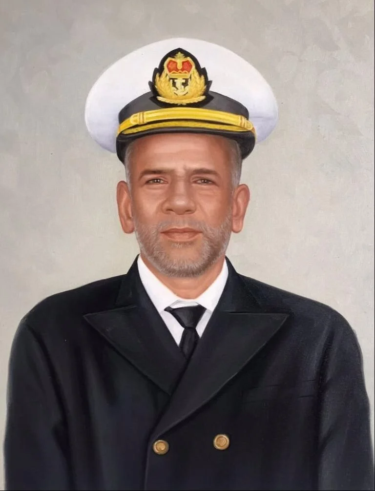 A man with a beard dressed in a black naval officer's uniform, wearing a white cap with a yellow and black emblem and gold trim, standing against a plain background.