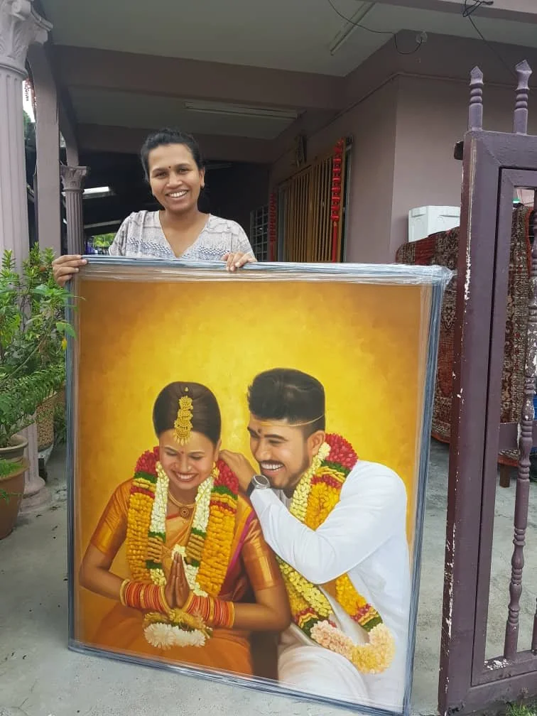 A woman standing outside, holding a large framed photo of a happy bride and groom dressed in traditional Indian wedding attire, smiling and looking at each other.