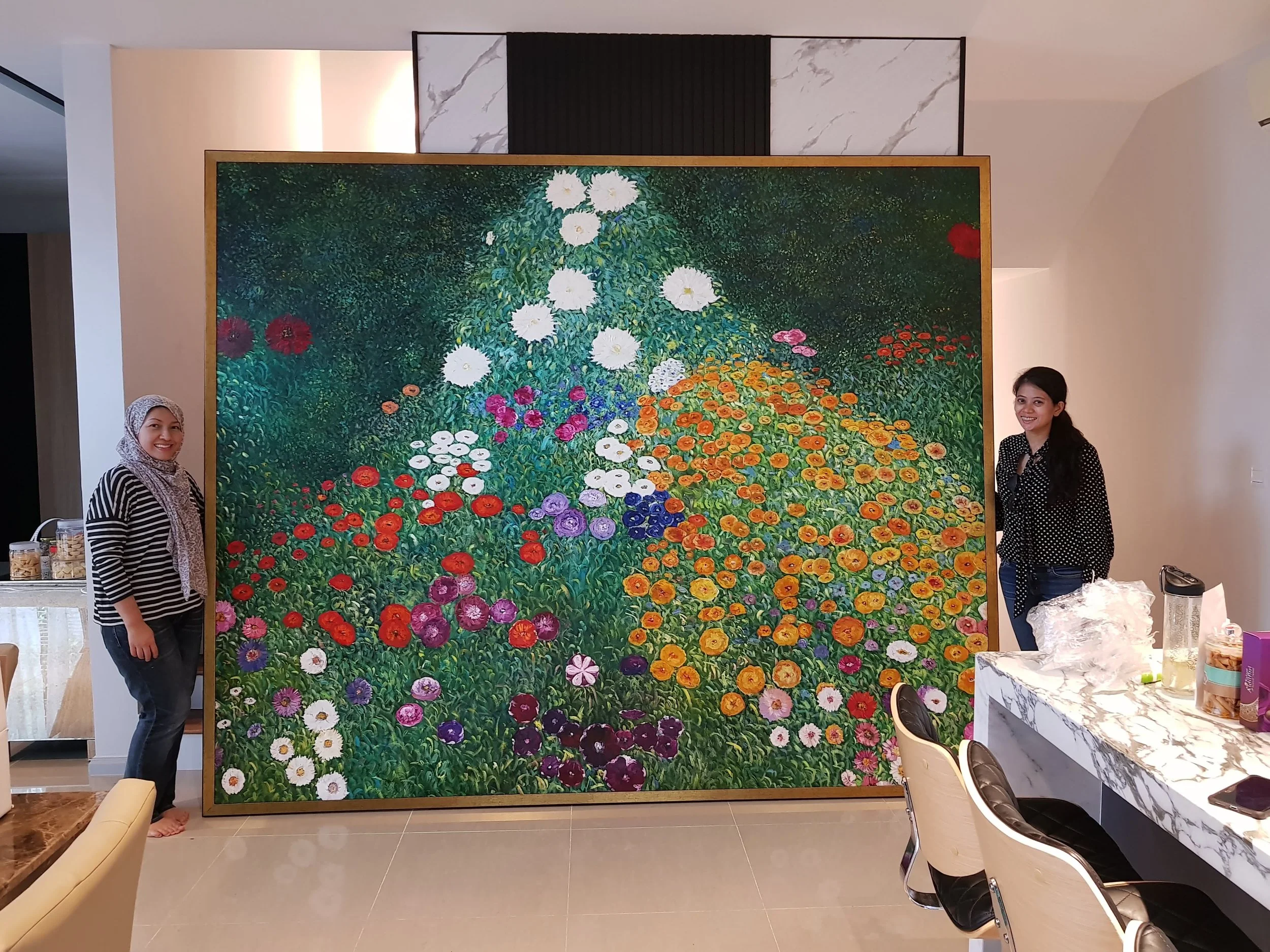 Two women standing on either side of a large painting of a colorful garden with various flowers in full bloom, displayed indoors.