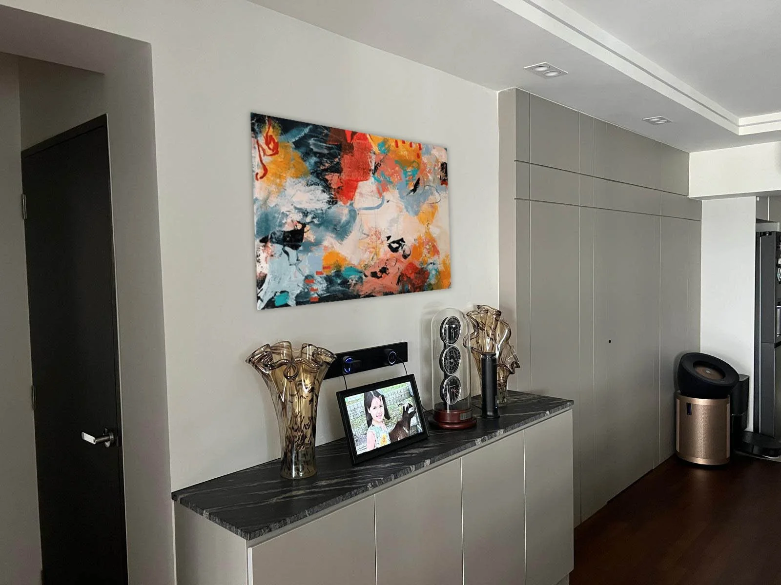 Interior of a modern living space with a white wall, abstract artwork, decorative vases, digital photo frame, and air purifier.