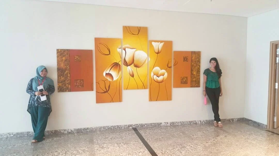 Two women standing on either side of a multi-panel floral painting on a white wall in an art gallery or museum.