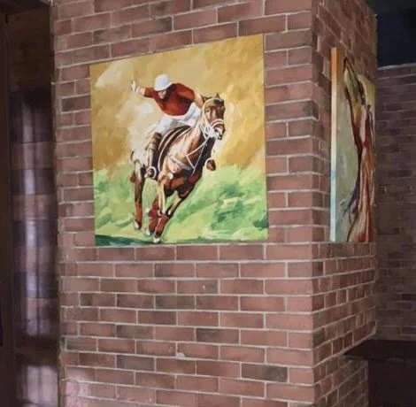 Painting of a jockey riding a horse on a brick wall.