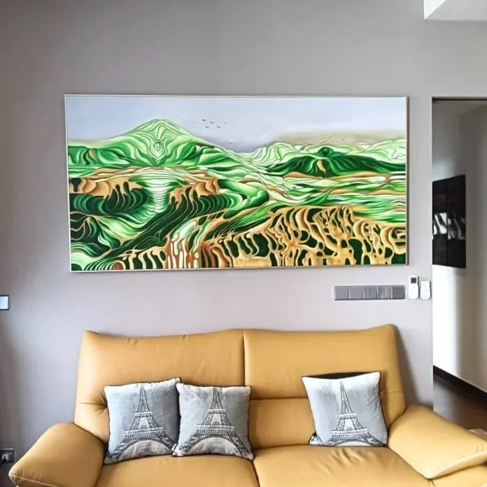 A living room with a tan couch, two pillows with Eiffel Tower designs, a large abstract landscape painting with green, brown, and tan colors on the wall, and a mounted TV on the side.