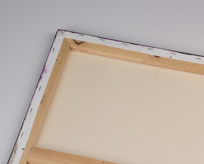 Close-up of the back of a blank canvas painting with a wooden frame, lying on a white surface.