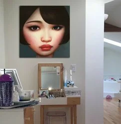 Close-up portrait of a woman with short black hair and makeup, displayed on a wall in a room.