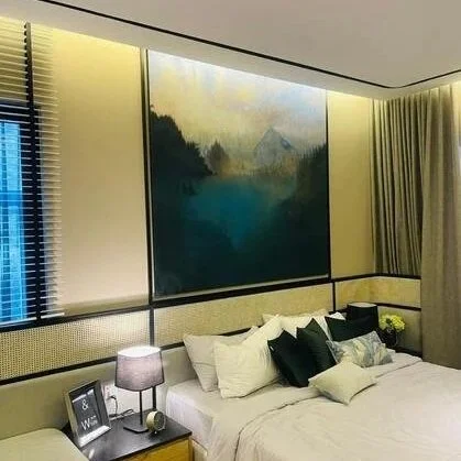 A bedroom with a large bed, multiple pillows, a nightstand with a lamp and some items, large curtains, and an abstract landscape painting on the wall.