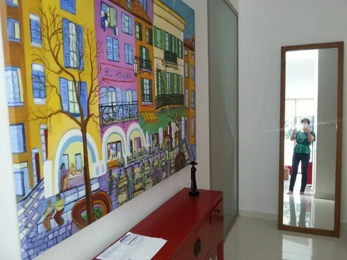 Room with colorful mural of buildings and trees, red sideboard, tall mirror, and a woman taking a photo in the reflection.