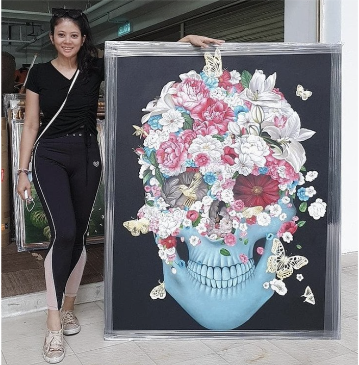 Woman standing next to a colorful skull artwork with flowers and butterflies painted on it.