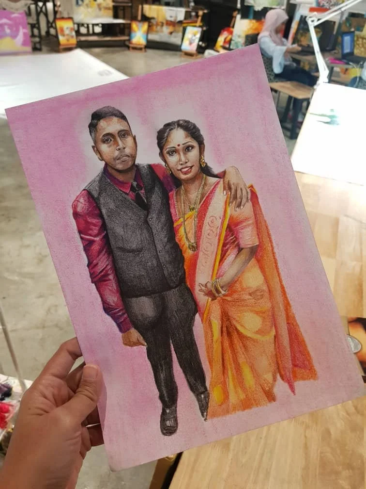 A hand holding a colorful portrait of a man and woman in traditional Indian attire, with a store or workshop in the background.
