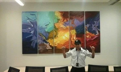 Person standing in front of a multi-panel abstract painting on a wall, with arms raised in a gesture.