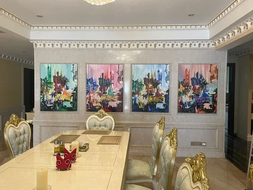 Elegant dining room with ornate chairs and a long table, decorated with candles and small decorative items. Four colorful abstract paintings hang on a wall behind the table.