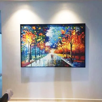 Colorful landscape painting of a park with trees in orange, yellow, green, and blue, a pathway, and two figures walking on the path, hanging on a white gallery wall.