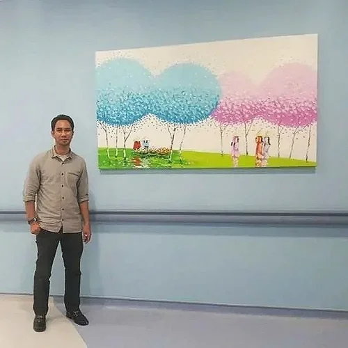 A man standing next to a colorful abstract painting with pastel trees and people, on a light blue wall.