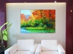 A vibrant landscape painting of autumn trees and a river hangs on a white wall in a modern living room with white sofas and a green plant.
