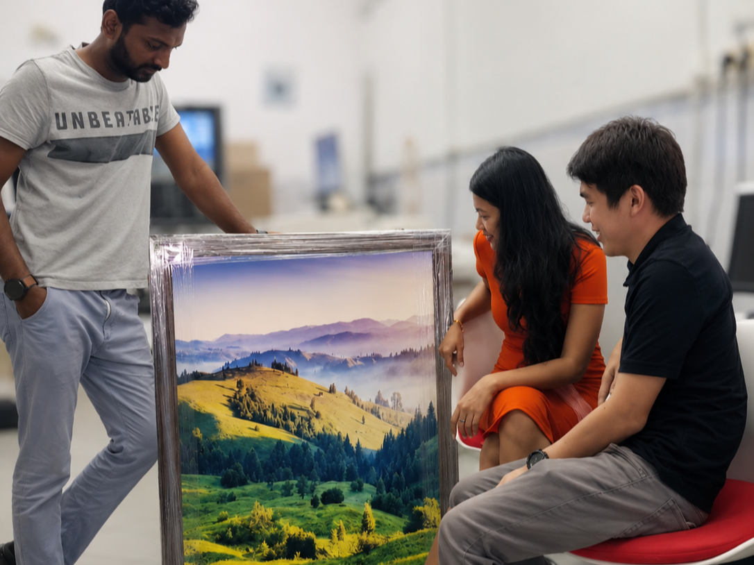 Three people in an art gallery looking at a landscape painting of rolling hills and mountains.