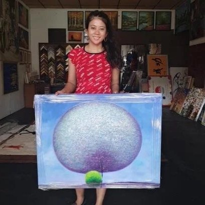 Young woman standing behind a painting of a tree and smiling.