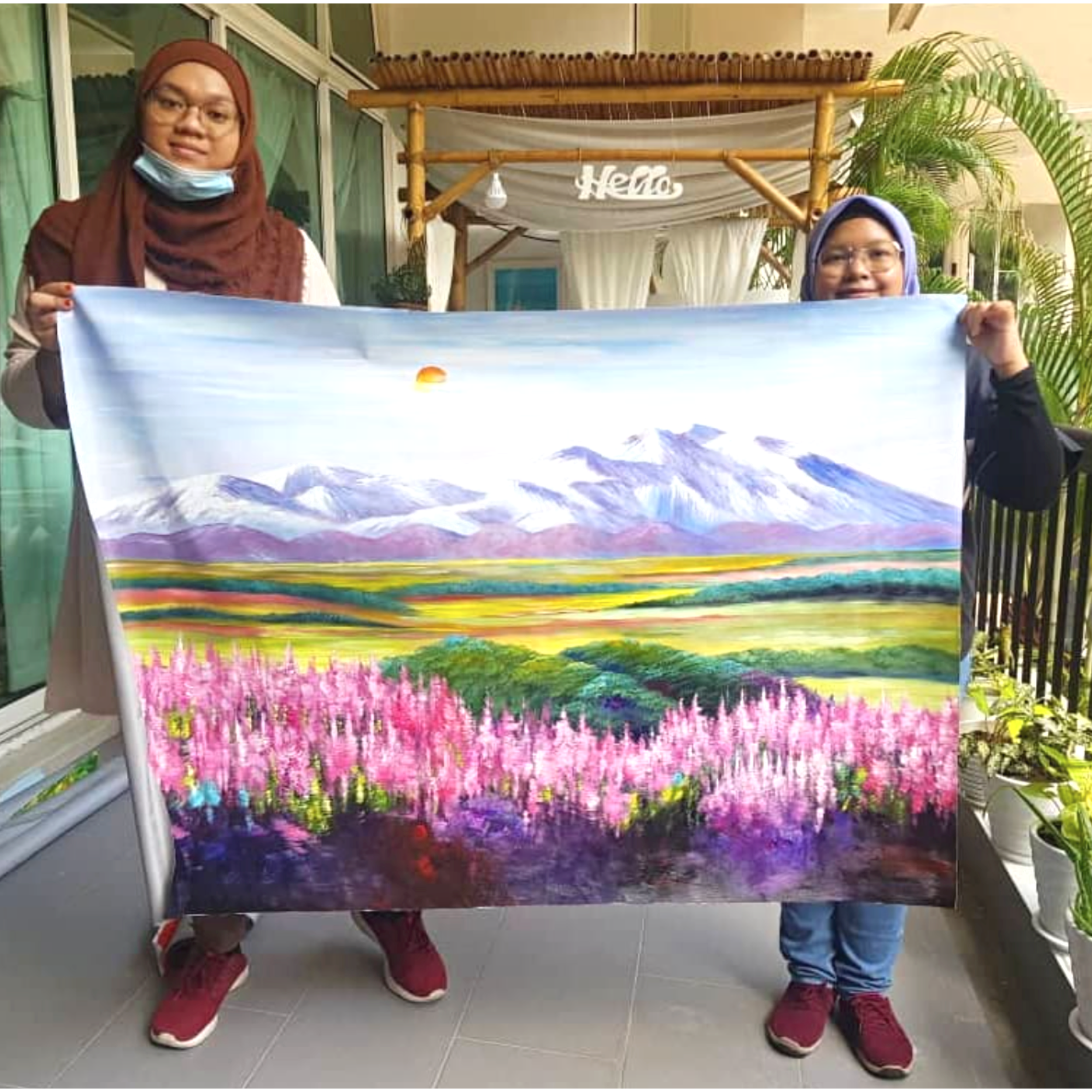 Two children, a girl and a boy, standing indoors holding up a large colorful painting of mountains, pink flowers, and a green landscape.