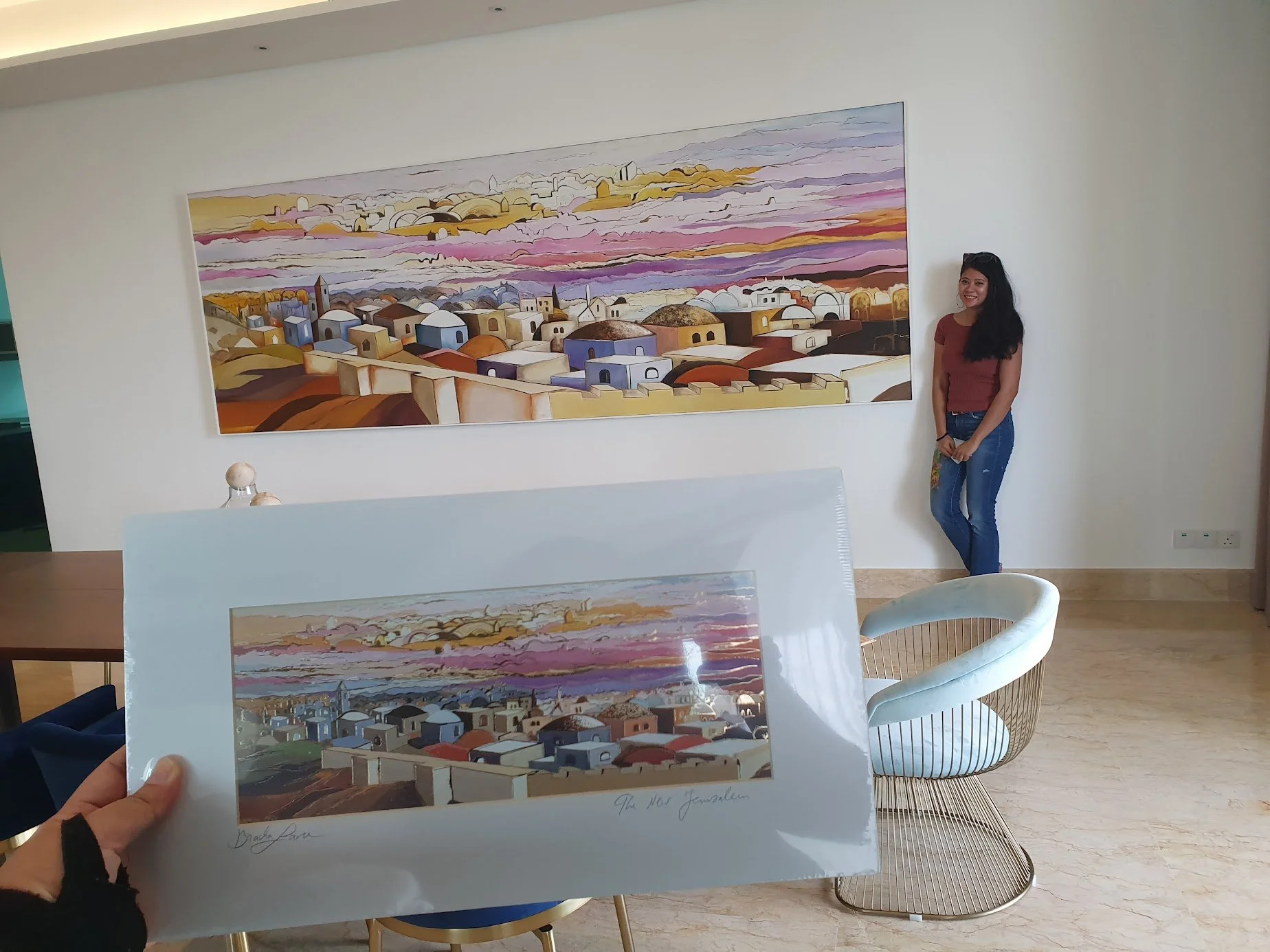 Photo of two paintings featuring colorful cityscape scenes, with a person standing next to the larger painting in a gallery setting.